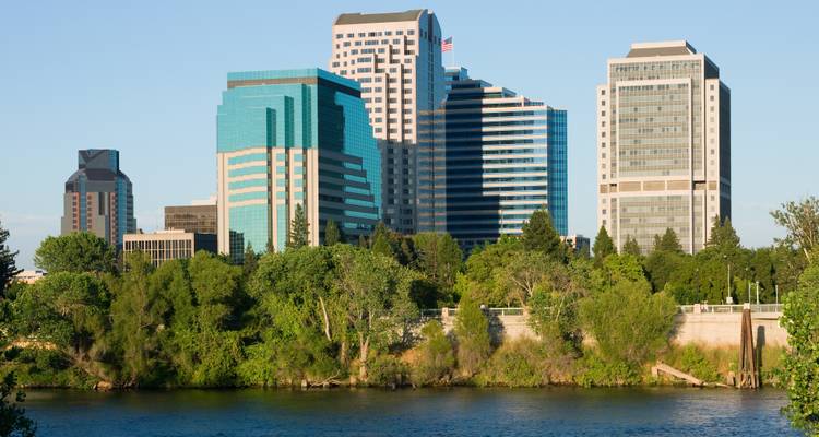 Die moderne Skyline von Sacramento erhebt sich hinter Bäumen entlang des American River an einem klaren Nachmittag.