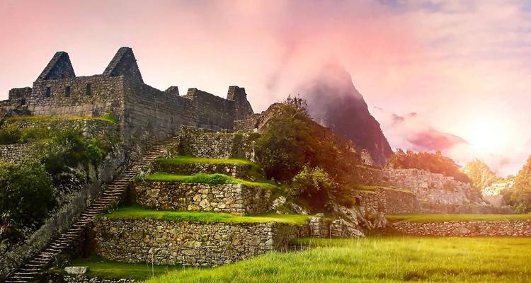 Las icónicas terrazas de piedra y templos de Machu Picchu brillan con la luz rosada del amanecer mientras la niebla se arremolina alrededor del pico Huayna Picchu.