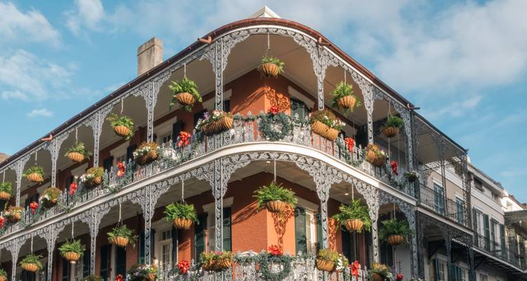 Historisches Gebäude mit schmiedeeisernen Balkonen, geschmückt mit hängenden Pflanzen unter hellem Himmel, typisch für das French Quarter von New Orleans.