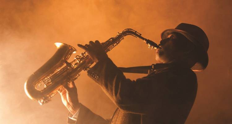 Silhouetted jazz saxophonist plays under warm, smoky stage lighting.