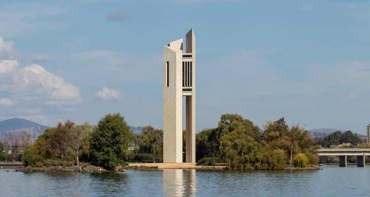 Tall, modern bell tower on an island in a lake.
