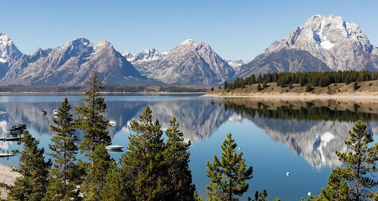 Die schneebedeckten Gipfel der Grand Tetons spiegeln sich perfekt in einem ruhigen Alpensee.