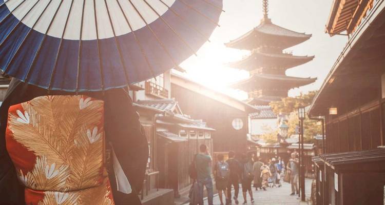 Personnage vêtu d'un kimono avec une ombrelle marchant dans une rue traditionnelle de Kyoto vers une pagode à cinq étages dans un rétroéclairage chaleureux.
