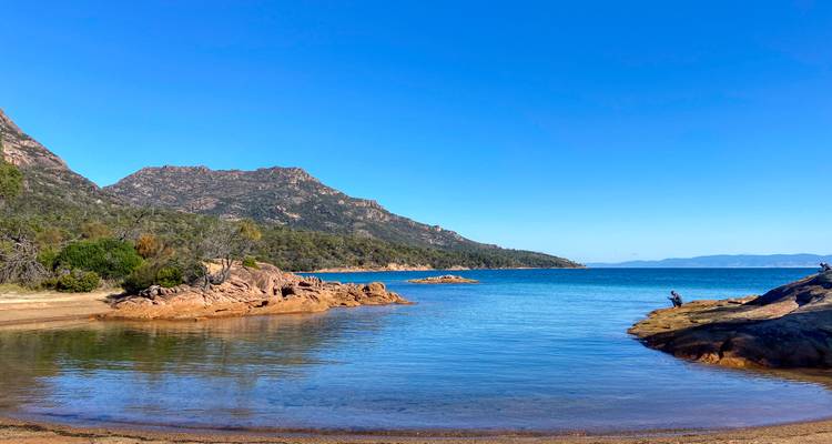 Ruhige türkise Bucht, gesäumt von felsigen Landzungen und niedrigen Bergen unter einem klaren blauen Himmel, mit einer kleinen sandigen Bucht im Vordergrund.
