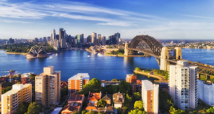 Wide cityscape of Sydney with bridge, Opera House and residential foreground on a bright day.
