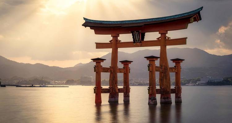 Torii emblématique dans l'eau avec un ciel dramatique et des montagnes en arrière-plan.