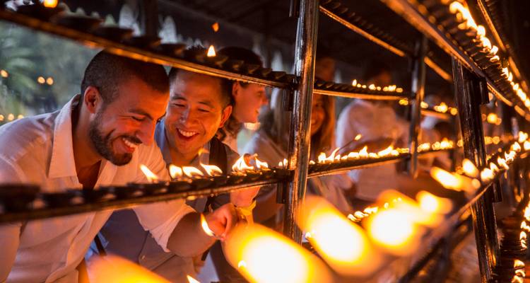 Visitors lighting rows of oil lamps in a dimly lit temple courtyard.