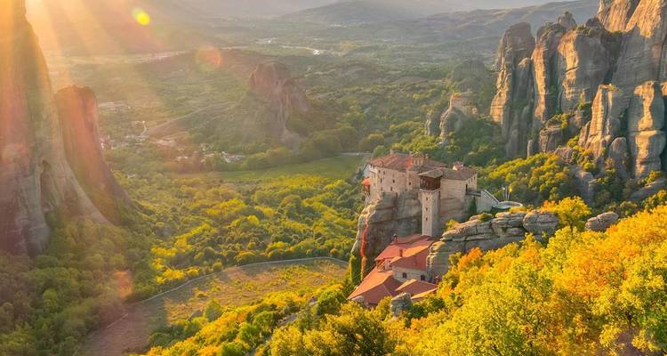 Une vue panoramique aux teintes dorées du coucher de soleil sur les imposants piliers rocheux de Météore, la vallée forestière et les monastères perchés sur les falaises