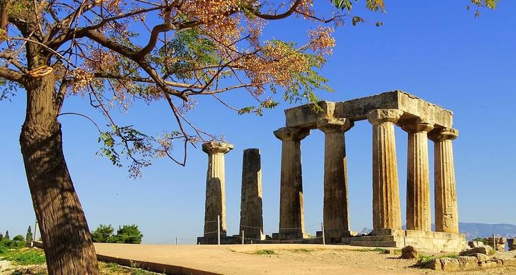 Ruines du Temple d'Apollon à l'Ancienne Corinthe encadrées par un arbre sur fond de ciel bleu éclatant
