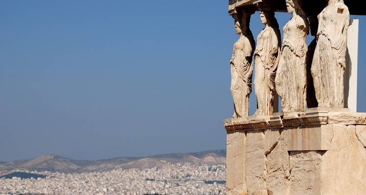 Statues on a building overlooking a sprawling cityscape in Athens.