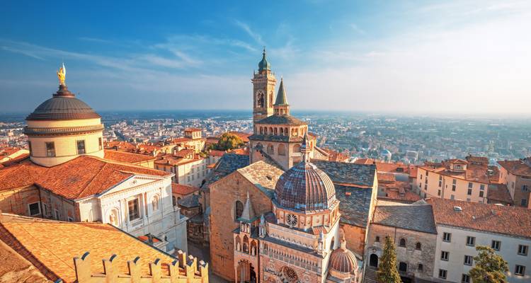 Sonnenbeschienene Hügelkuppen-Skyline von Bergamos Città Alta mit Renaissance- und mittelalterlichen Türmen, Kuppeln und Terrakottadächern mit Blick über die Ebenen.