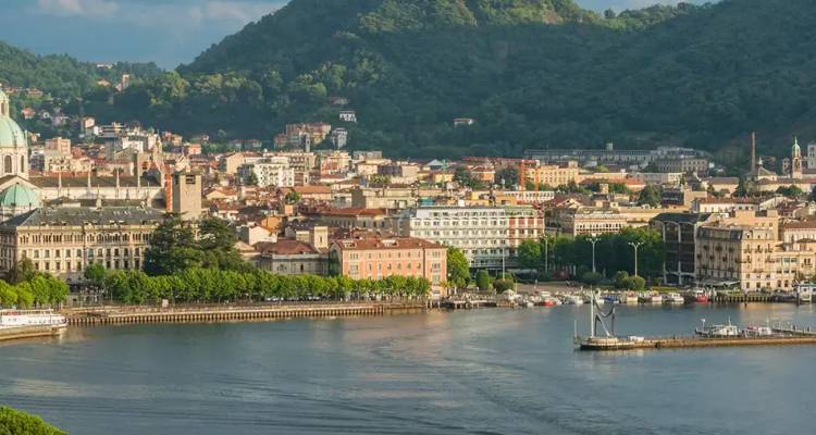 Vista panorámica del paisaje urbano a orillas del lago de Como respaldado por colinas exuberantes bajo un cielo al atardecer.