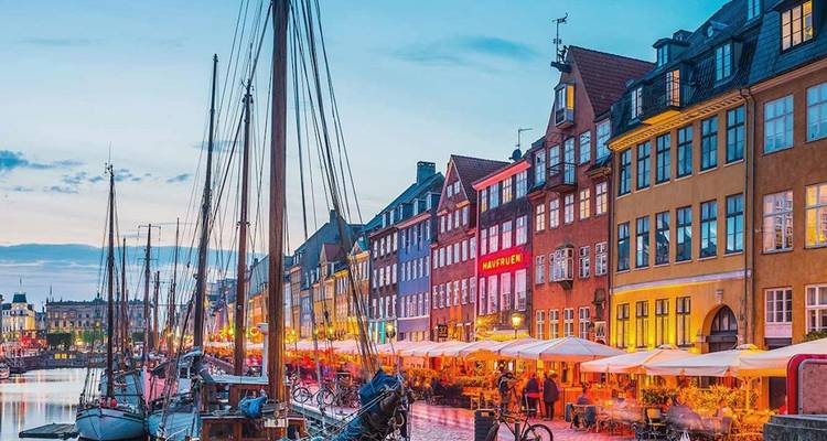 Vista nocturna del colorido canal Nyhavn de Copenhague bordeado de barcos y cafés animados.