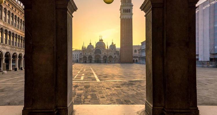 Ausblick auf den Markusplatz und die Markusbasilika bei Sonnenaufgang, gerahmt von Steinbögen in Venedig.