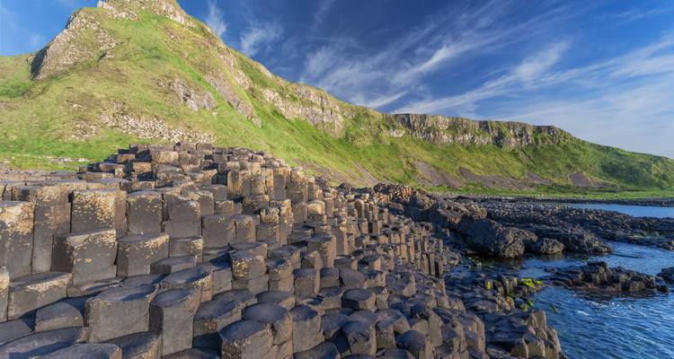 Sechseckige Basaltsäulen des Giant's Causeway, die zu grünen Klippen und blauem Meer führen.
