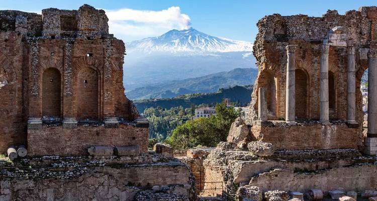 Ruines d'un théâtre romain antique avec une montagne en arrière-plan.