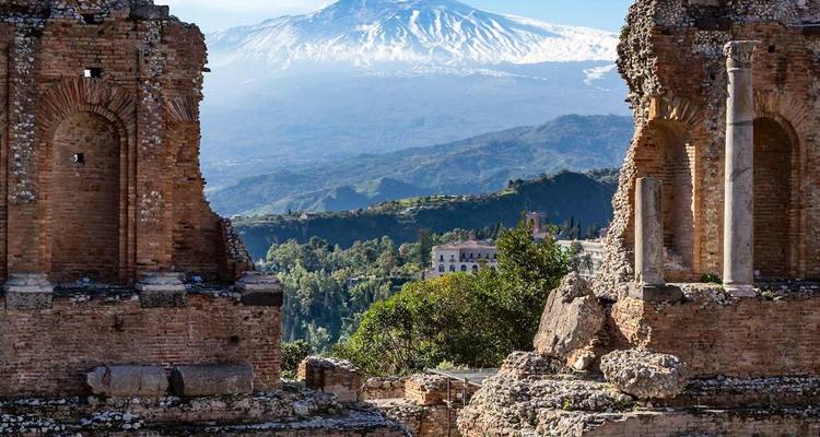 Las ruinas de un antiguo teatro de ladrillo enmarcan el Monte Etna coronado de nieve alzándose en la distancia.