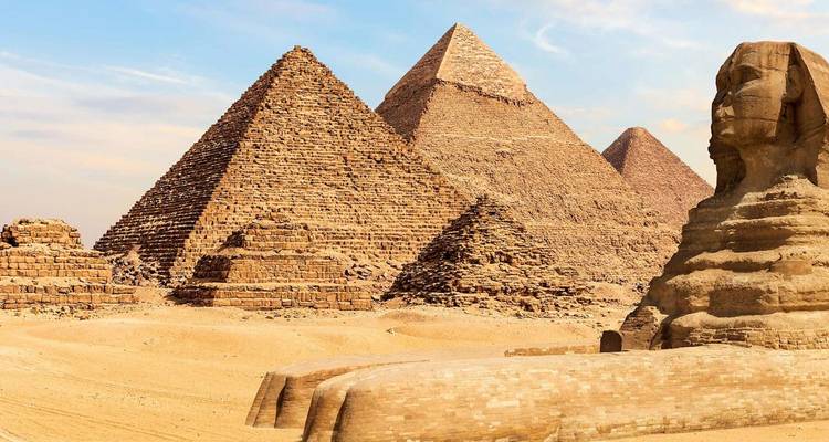Las Grandes Pirámides de Giza y la Esfinge bañadas en luz dorada del desierto bajo un cielo azul.