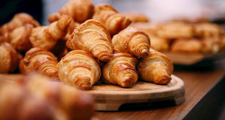 Bord opgestapeld met versgebakken croissants, focus op voorste rij gebakjes.