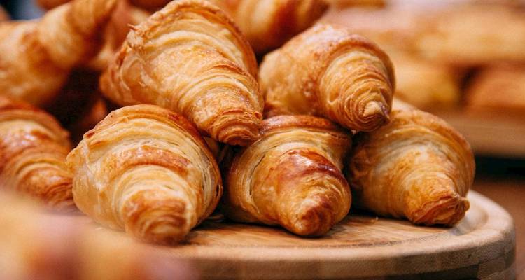 Croissants dorados recién horneados están apilados en una bandeja de madera