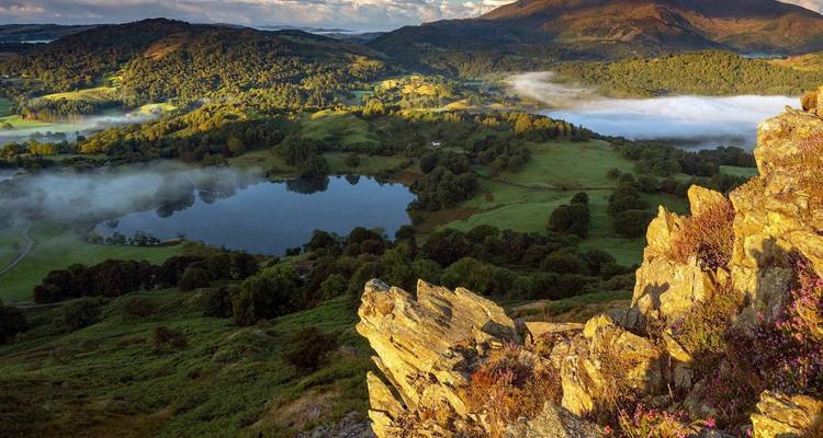 Collines brumeuses et un lac serein reflétant le paysage environnant dans le Lake District.