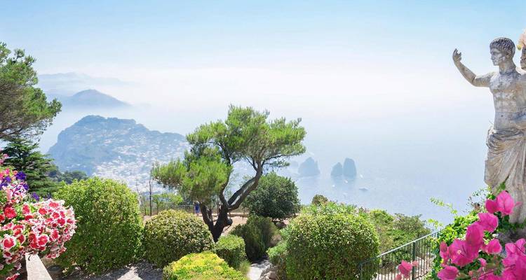 Vista panorámica sobre los acantilados de Capri y los Faraglioni enmarcados por flores coloridas y una estatua clásica.