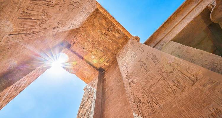 Anciennes colonnes de pierre avec des sculptures sous un soleil éclatant.