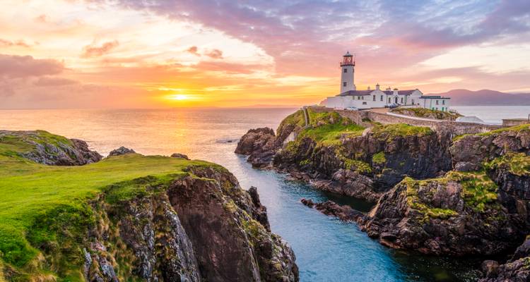 Fanad Head Leuchtturm auf zerklüfteten Klippen, erleuchtet von einem lebendigen Küstensonnaufgang in County Donegal.