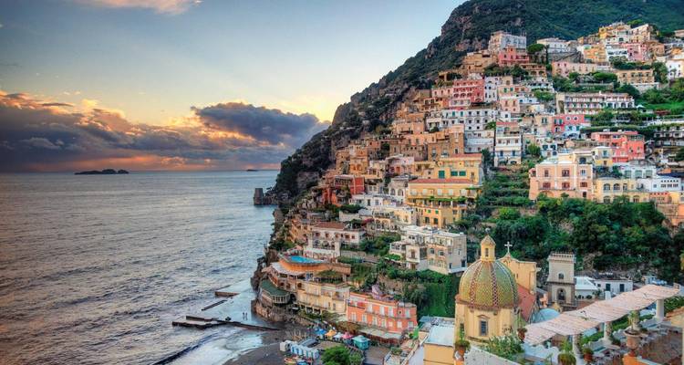 Village coloré à flanc de falaise avec des bâtiments pittoresques au bord de la mer, au lever ou au coucher du soleil.