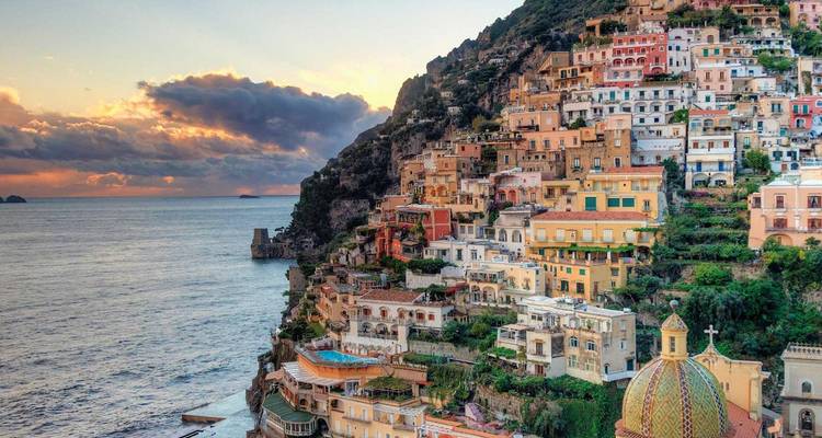 Colorful cliffside houses of Positano cascade toward the Mediterranean at sunset with dramatic clouds.
