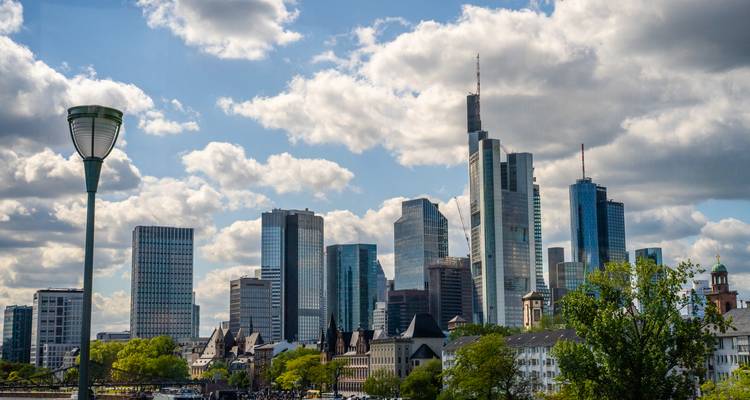 Tageshimmel von Frankfurt mit modernen Wolkenkratzern, eingerahmt von belaubten Bäumen.