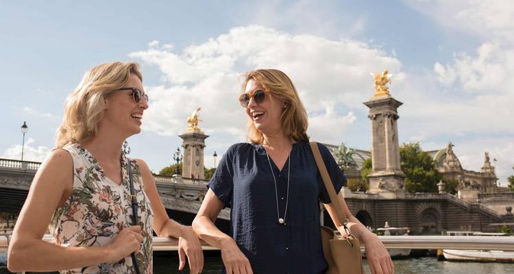 Deux femmes qui rient sur un pont avec des statues dorées.