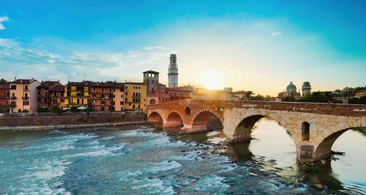 A historic stone bridge over a river with buildings and a church tower.