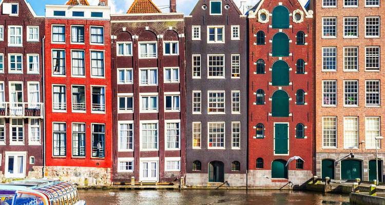 Les maisons de canal peintes de couleurs vives se reflètent dans l'eau calme sous un ciel ensoleillé.