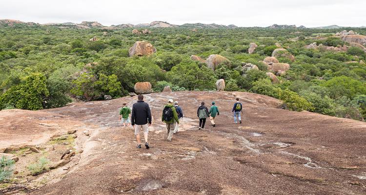Les randonneurs traversent une large dalle de granit surplombant le parc national de Matobo, parsemé de rochers et verdoyant.