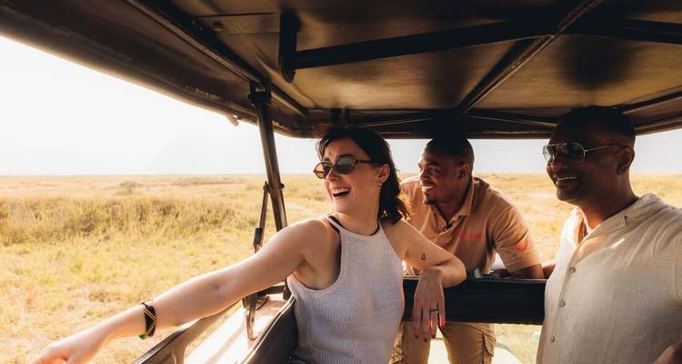 Fröhliche Reisende stehen in einem offenen Safarifahrzeug und durchsuchen die Savanne.