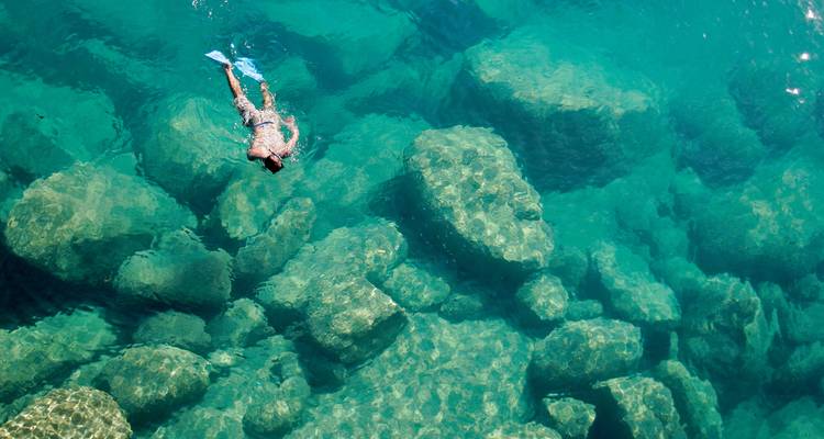 Eine Person, die in kristallklarem Wasser über Felsen schnorchelt.