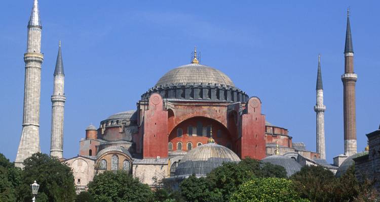 Iconic Hagia Sophia with its minarets rises majestically against a clear blue Istanbul sky framed by greenery.