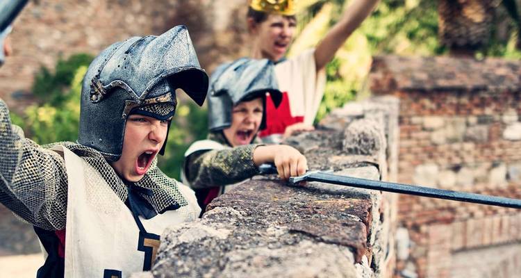 Des enfants enthousiastes déguisés en chevaliers médiévaux brandissent des épées en jouet sur un rempart de château.