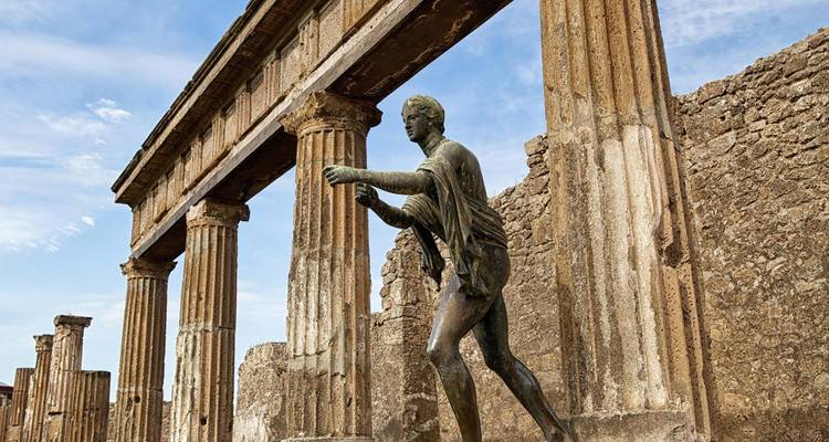 Ruines antiques avec des colonnes de marbre et une statue par une journée ensoleillée.