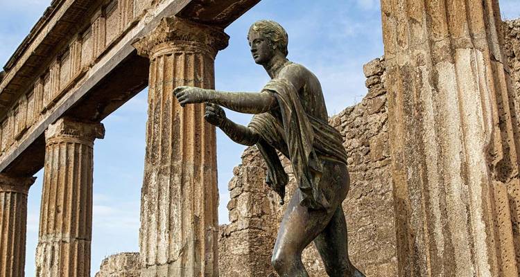 Una estatua de bronce se alza entre las columnas desgastadas de un antiguo templo romano.
