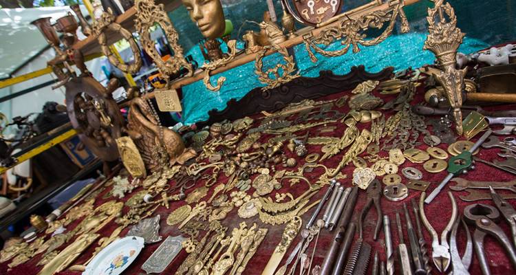 Mesa del mercadillo de antigüedades llena de curiosidades de latón ornamentado, llaves y herramientas vintage sobre un paño rojo.
