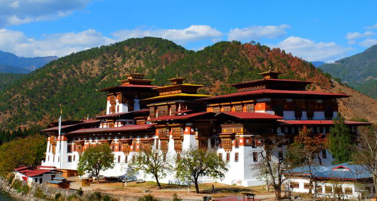 A large dzong with red roofs against a mountain backdrop.
