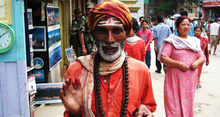 A smiling man in traditional attire with bustling street activity in the background.