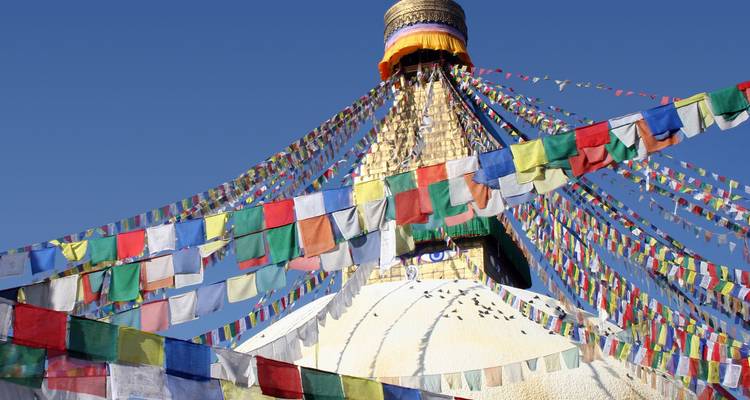 Boudhanath Stupa crowned with prayer flags fluttering against a clear blue sky.