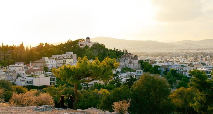 Deux personnes sont assises sous un arbre avec une vue sur Athènes à l'heure dorée et chaleureuse