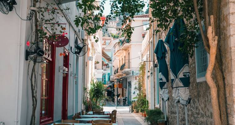 Charmante ruelle étroite bordée de tables de café, de fleurs et de bâtiments grecs traditionnels