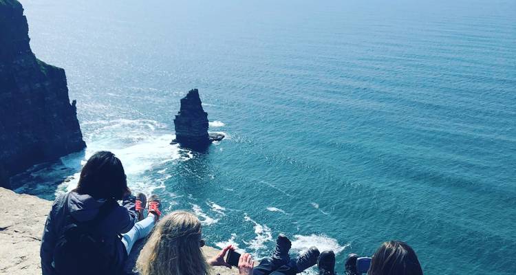 Mensen die op de rand van een klif zitten met uitzicht op de zee.