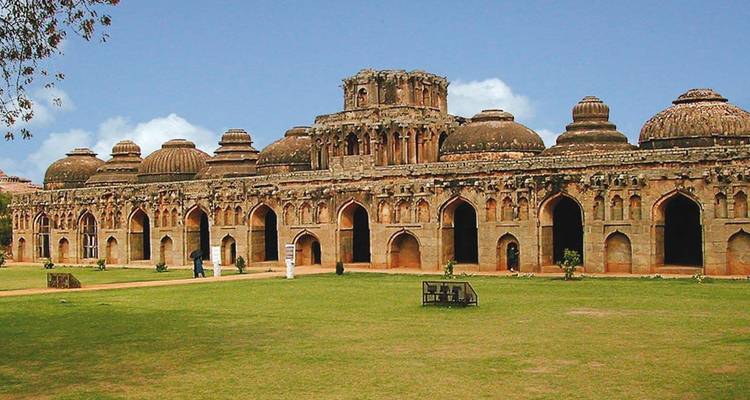 El gran complejo de Establos de Elefantes con cúpula en Hampi se encuentra en un jardín bien cuidado bajo un cielo azul.