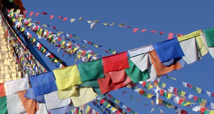 Kleurrijke gebedsvlaggetjes die wapperen tegen een heldere blauwe lucht.